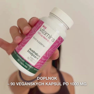 Detail ruky, ktorá drží fľaštičku výživového doplnku Vitamin B12, otvára viečko a vysypáva hladké biele kapsuly – produkt určený na každodenné užívanie pre podporu energie, imunity, nervového systému a zníženie únavy.