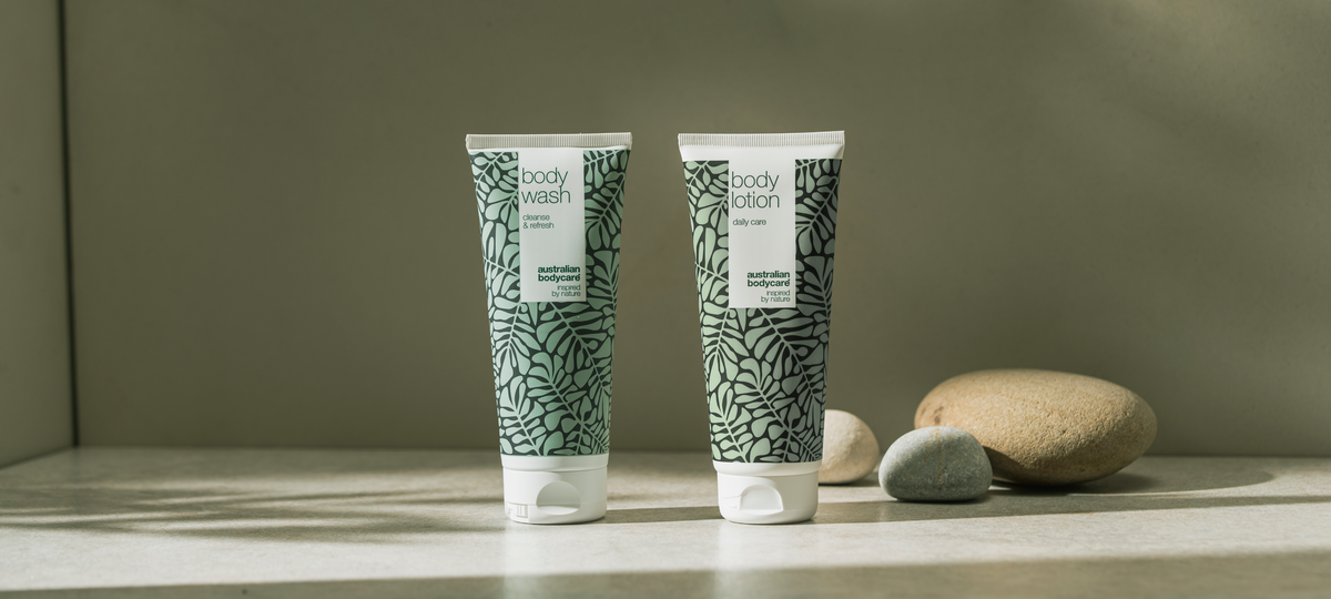 Body Wash a Body Lotion od Australian Bodycare v zelenom dizajne s tea tree na svetlom kamennom povrchu, vedľa hladké okruhliaky.