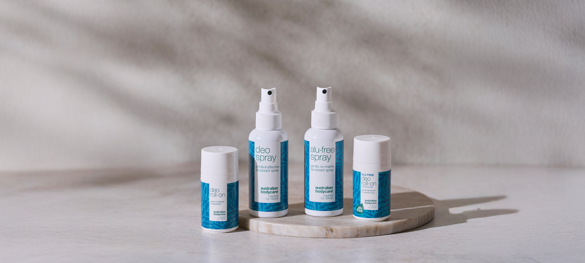 Štyri dezodoranty od Australian Bodycare na okrúhlej mramorovej doske: Deo Roll-on, Deo Spray, Alu-free Spray a Alu-free Deo Roll-on v bielo-modrom obale.