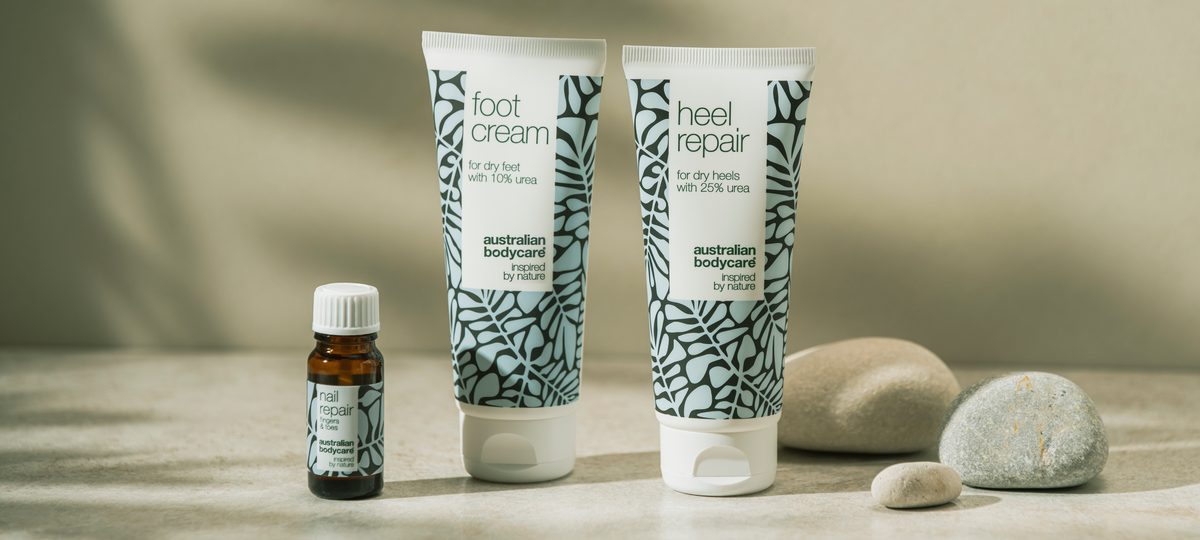 Fľaštička oleja Nail Repair, Foot Cream a Heel Repair od Australian Bodycare vo svetlomodrom obale na kamennom povrchu, vedľa okruhliaky.