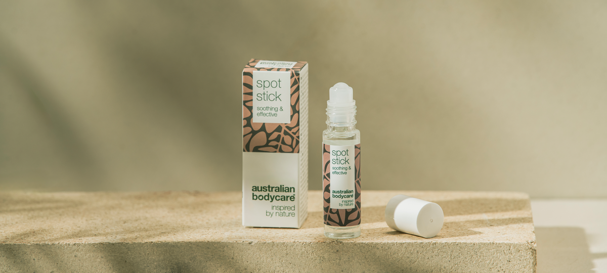 Roll-on Spot Stick od Australian Bodycare vedľa béžovej škatuľky na kamennom kvádri, uzáver leží vedľa.
