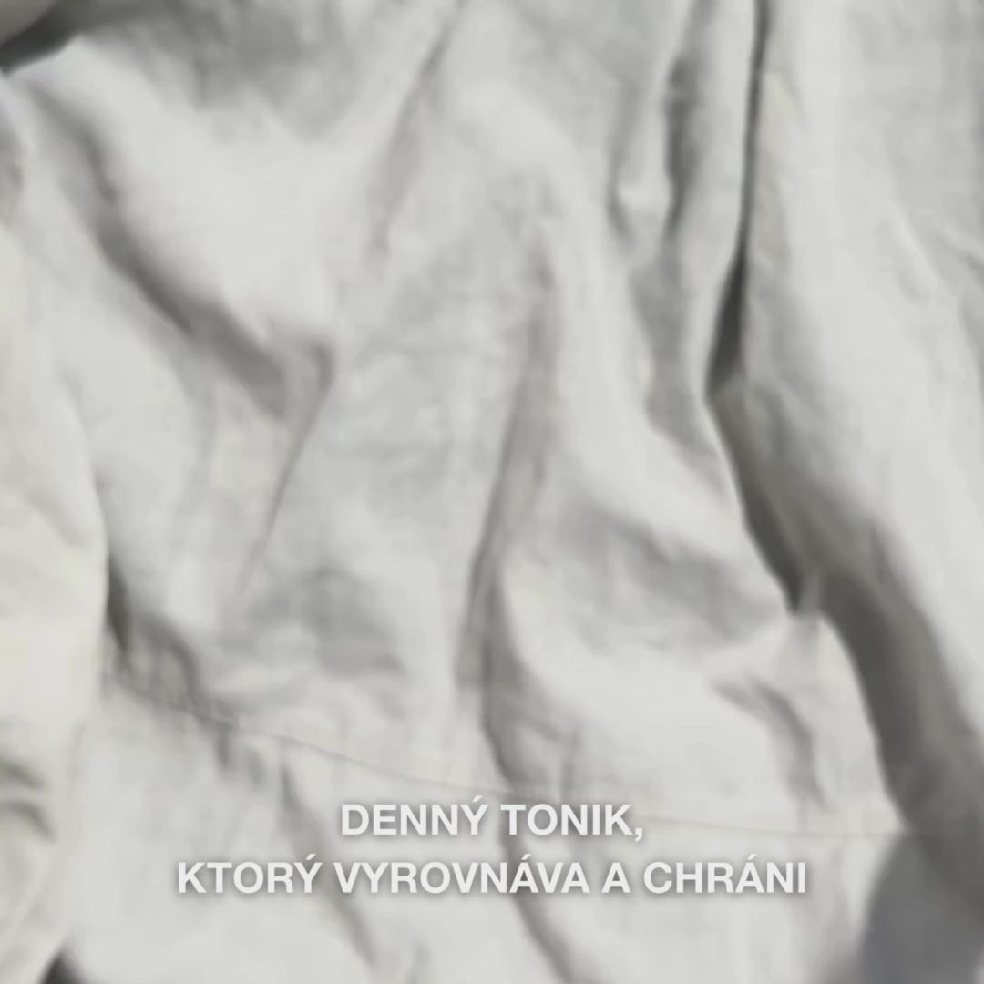 Detail ruky, ktorá nakvapká niekoľko kvapiek číreho, vodnatého Face Tonic s tea tree olejom na tampónik a potom ho jemne potiera po čistej pokožke tváre: ľahká, osviežujúca tekutina upokojuje, hlboko čistí, hydratuje a zanecháva pleť obnovenú a pripravenú na krém.