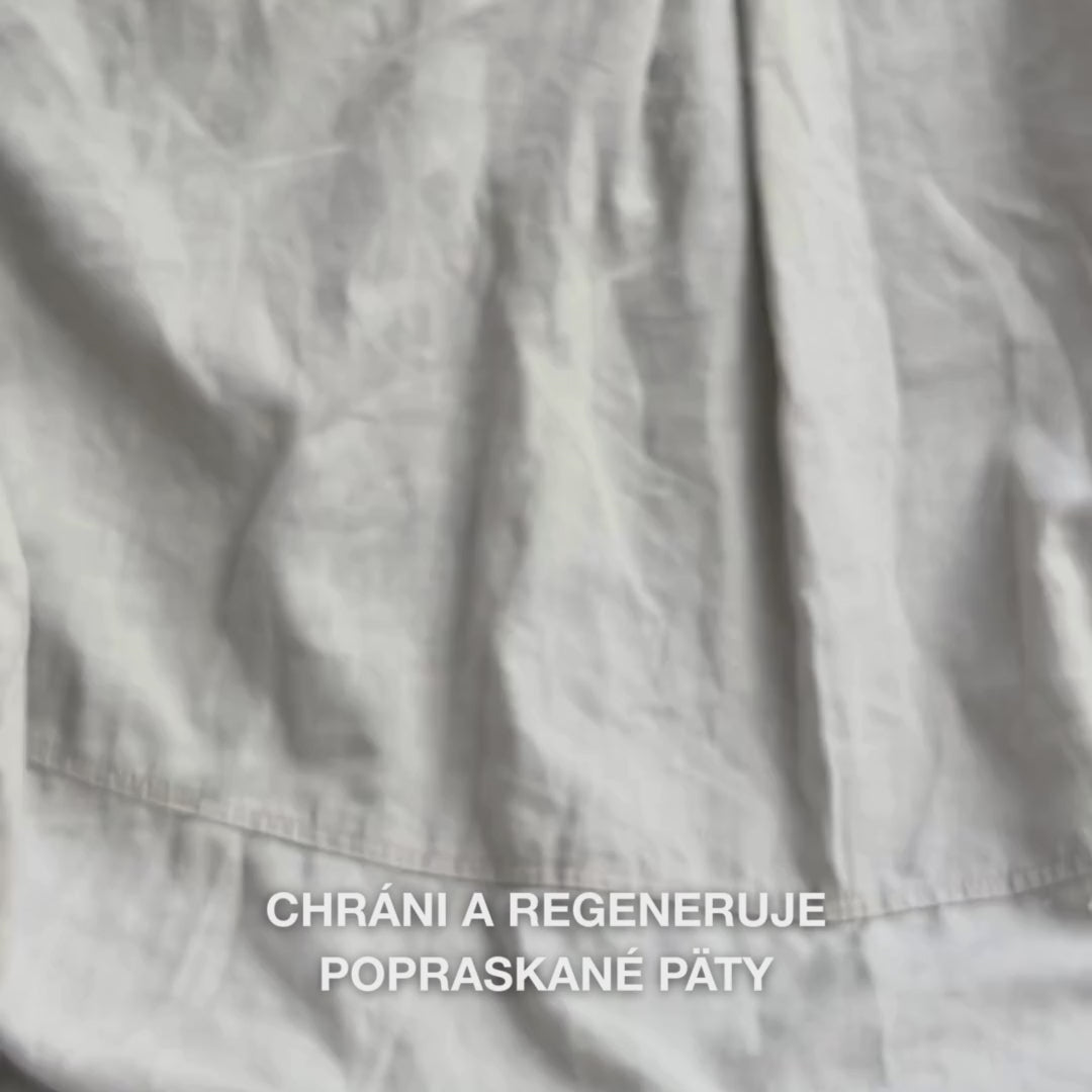 Detail ruky naberajúcej bohatú, krémovú textúru Heel Repair do dlane a jemne ju vmasírovávajúcej do suchej, popraskanej pokožky päty: hustá konzistencia sa viditeľne vstrebáva, zmäkčuje a hydratuje drsné miesta, pričom 25 % močovina, bambucké maslo a tea tree olej upokojujú a chránia pokožku.