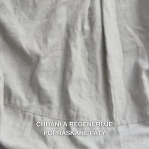 Detail ruky naberajúcej bohatú, krémovú textúru Heel Repair do dlane a jemne ju vmasírovávajúcej do suchej, popraskanej pokožky päty: hustá konzistencia sa viditeľne vstrebáva, zmäkčuje a hydratuje drsné miesta, pričom 25 % močovina, bambucké maslo a tea tree olej upokojujú a chránia pokožku.